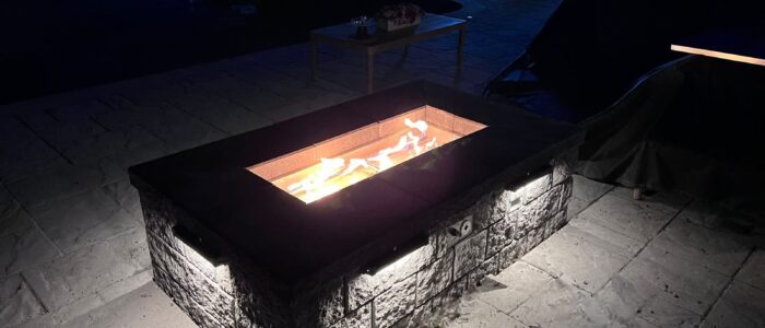 Custom gas fire pit burning at night on a Barrie backyard patio