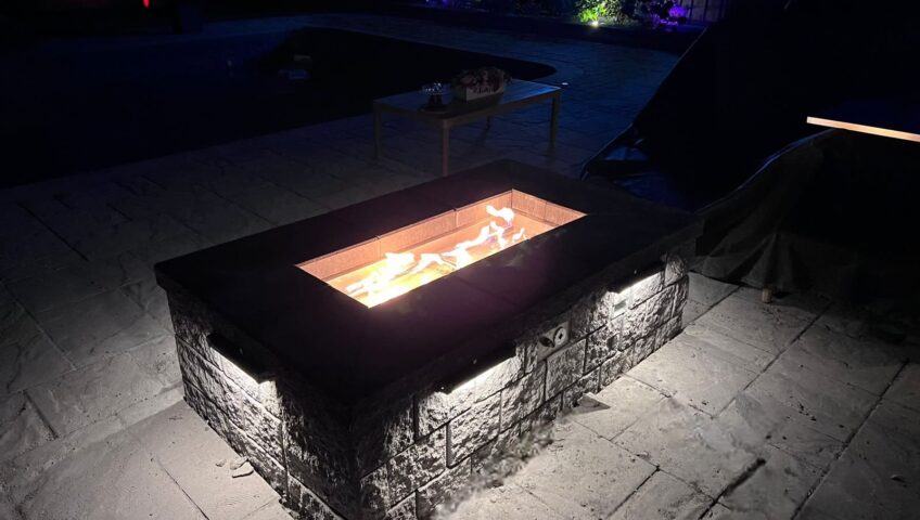 Custom gas fire pit burning at night on a Barrie backyard patio