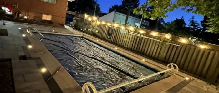 Backyard pool at night with interlocking patio and landscape lighting, Barrie