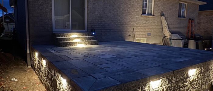 Raised interlocking patio with retaining wall and LED lighting at night, Barrie